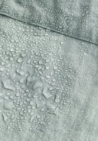 Waterbestendige stof in een lichtgrijze kleur, met talrijke kleine waterdruppels op het gestructureerde oppervlak.