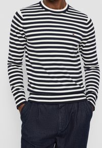 Marinblå och vit randig långärmad stickad tröja med rundad halsringning och ribbade ärmslut, i kombination med mörka denimbyxor.