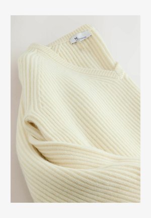 Cream-colored ribbed knit sweater with a V-neck, featuring a soft texture and a label at the neckline.