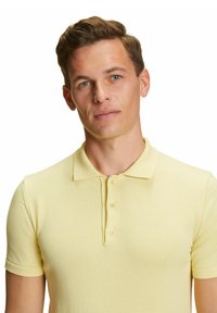 Polo shirt giallo in cotone con texture a coste, maniche corte e colletto classico con tre bottoni sul davanti.