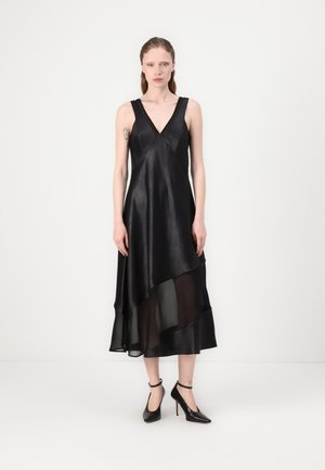 Black dress with a V-neck, layered design, and sheer bottom hem. Made from a smooth fabric, paired with black high-heeled shoes.