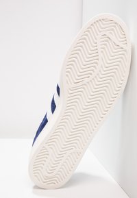 Blue suede sneaker with a white rubber sole featuring a zigzag tread pattern. Three white stripes adorn the side for contrast.