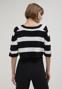 Gestreifter schwarzer und weißer Crop-Pullover mit weitem Ausschnitt und kurzen Ärmeln, hergestellt aus einem weichen Strickmaterial und mit lockerer Passform.