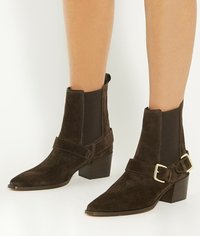 Bottines en daim marron avec un bout pointu, des panneaux élastiques sur les côtés et une sangle à boucle au niveau de la cheville. Le talon-block ajoute de la stabilité.