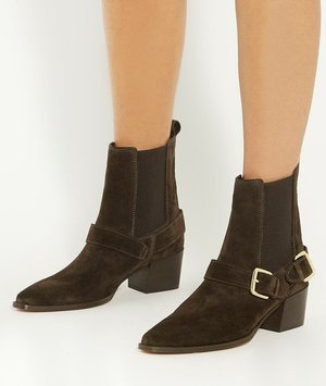 Bottines en daim marron avec un bout pointu, des panneaux élastiques sur les côtés et une sangle à boucle au niveau de la cheville. Le talon-block ajoute de la stabilité.
