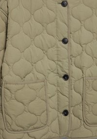 Lekka oliwkowa pikowana kurtka z falistym przeszyciem, zapięciem na guziki z przodu oraz dwoma dużymi naszywanymi kieszeniami.