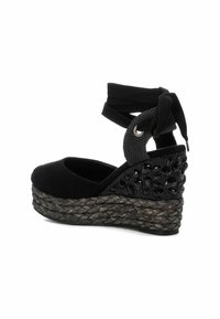 Sandalias de cuña negras con parte superior de ante, con cuentas decorativas en el lateral y una plataforma de yute trenzado. Correa en el tobillo para un ajuste seguro.