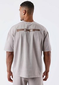 Camiseta de algodón gris con mangas cortas y un corte relajado, con un gran logo marrón "PXP" estampado en la parte posterior.