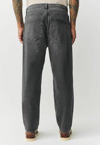 Grå denimjeans med et lige ben snit, to baglommer og et rent design. Stoffet har en subtil tekstur, kombineret med brune sko.