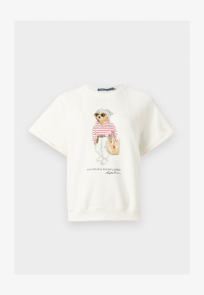 Λευκό φούτερ με κοντά μανίκια με μια αρκούδα που φοράει γυαλιά ηλίου, ριγέ πουκάμισο, λευκό παντελόνι, μαντήλι στο κεφάλι και κρατά τσάντα tote, τυπωμένο στο μπροστινό κέντρο.