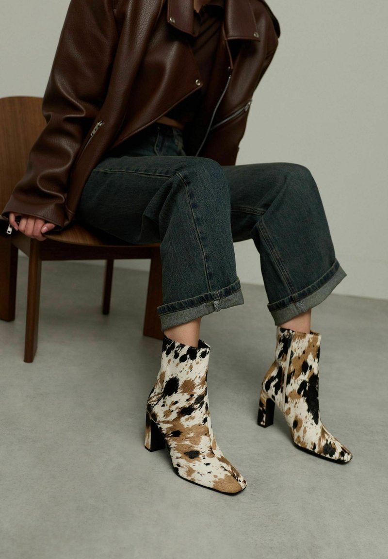 Bottes à cheville en imprimé vache avec un talon carré. Fabriquées en tissu avec des taches noires, brunes et crème, elles présentent un bout pointu et un dessus ajusté.