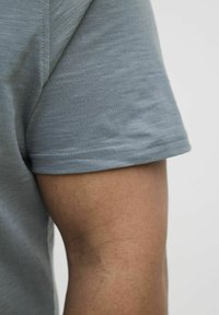 Chemise à manches courtes bleu clair en tissu doux, avec un col rond et un ourlet soigneusement cousu, montrant un gros plan de la manche.