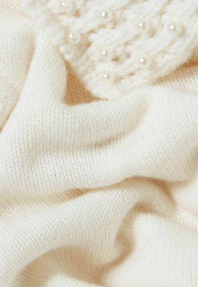 Tejido blanco de punto con una textura suave, que presenta una sección decorativa con acentos de perlas y un aspecto suave y cálido.