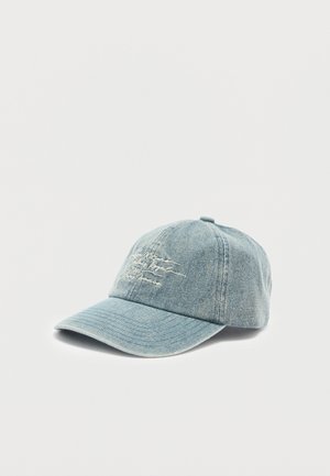 Gaiši zila džinsa beisbola cepure ar izliekto malu un baltu kursīvu izšuvumu priekšējā panelī, uz vienkārša balta fona.