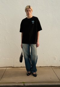 Black oversized t-shirt with a small colorful graphic, light blue faded wide-leg jeans, black pointed shoes, and a small black handbag.