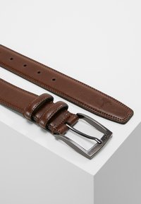 Ceinture en cuir marron avec une texture lisse, dotée d'une boucle en métal argenté, de trois boucles ajustables et d'un emblème de marque discret.
