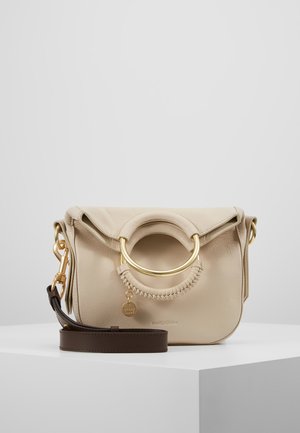 Bolso de cuero beige con un prominente asa circular dorada, que presenta un detalle cosido y una correa marrón ajustable.