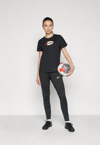 Svart t-skjorte med "aimax"-logo, sammen med tettsittende svarte bukser med teksturerte detaljer, og en mønstret fotball.