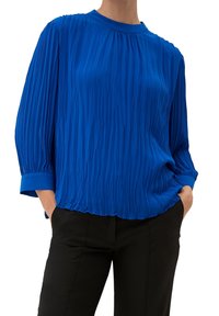 Blusa blu a pieghe con scollatura rotonda e maniche lunghe. Realizzata in materiale leggero, presenta una superficie testurizzata e una vestibilità rilassata.