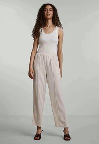 Débardeur blanc côtelé avec un pantalon beige clair à jambes larges. Le tissu semble doux, avec une coupe décontractée et une taille froncée. Des sandales plates complètent le look.