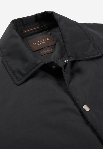 Czarna kurtka z kołnierzem, zapinana na zatrzaski, z widocznymi brązowymi metkami z napisem "Slowear Montedoro" i "Teknosartorial".