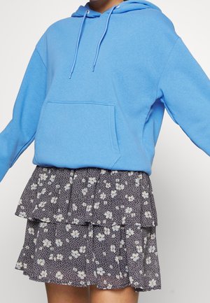 Person wearing a light blue hoodie with front pocket and drawstrings paired with a black floral tiered skirt.