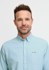 Camicia azzurra chiara con colletto, maniche lunghe e taschino sul petto con un accento a righe multicolori. Tessuto morbido.