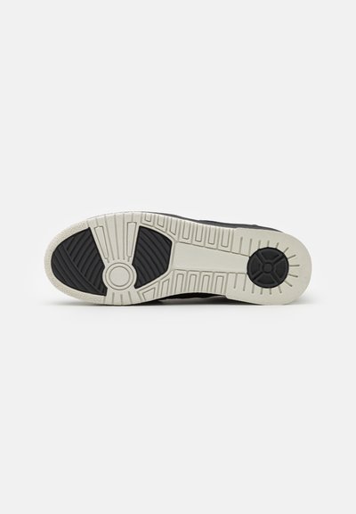 Black sneaker outsole featuring a textured rubber design with a contrasting white midsole and patterned tread for traction.