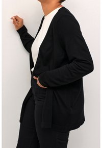 Sort cardigan, �åben frontdesign, lange ærmer, blød strikstruktur, parret med en hvid top og sorte bukser, minimalistisk stil.