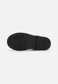 Suela de goma negra con un patrón de agarre texturizado, que presenta surcos profundos y un detalle central circular. Duradera y diseñada para ofrecer tracción.