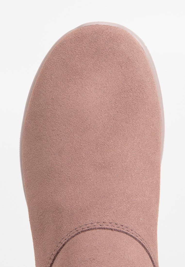 Detailaufnahme der abgerundeten Schuhspitze eines staubigen rosa Wildlederschuhs mit sichtbaren Nähten entlang der Kante.