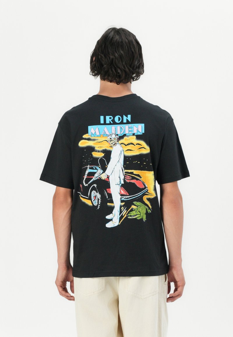 Tricou negru din bumbac, cu un graphic retro pe spate, reprezentând un personaj lângă o mașină, cu accente colorate și textul "IRON MAIDEN."