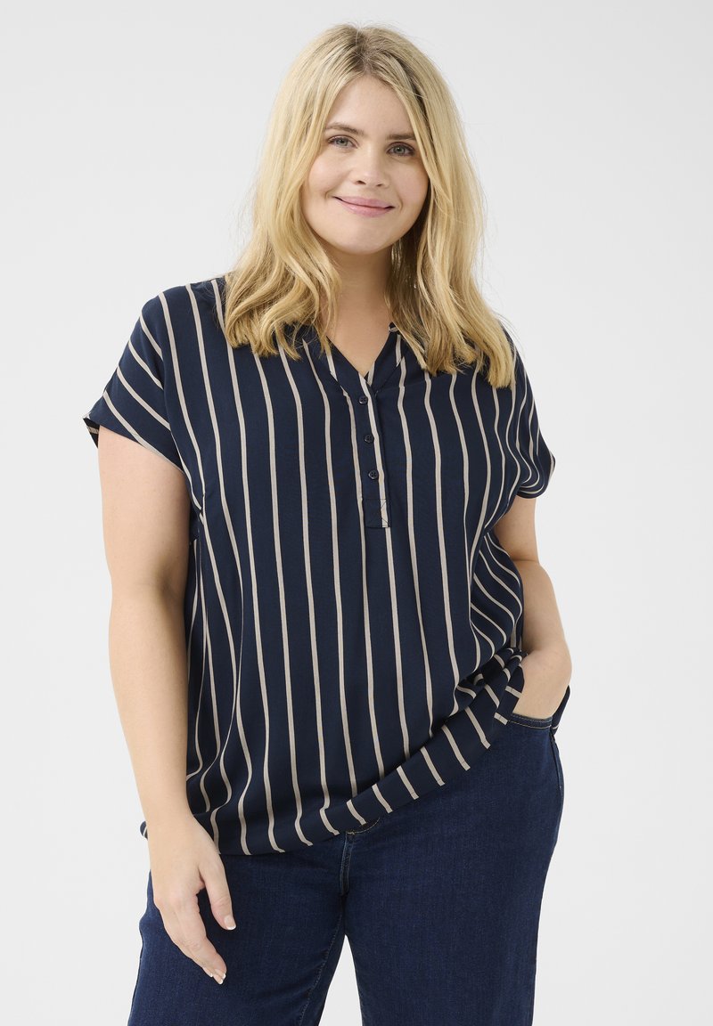 Blouse bleu marine à manches courtes avec des rayures verticales beiges, un col en V boutonné et une coupe décontractée, associée à un jean foncé.
