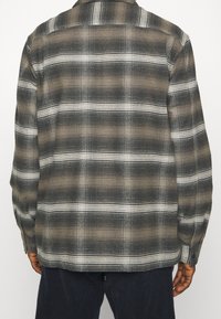 Rutigt flanellskjorta i grå och vita nyanser med knappkrage. Mjuk textur, långa ärmar och en rak nederkant.