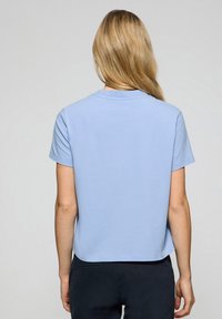 T-shirt en coton bleu clair avec des manches courtes et un col rond. L'ourlet est légèrement court et le tissu semble lisse et doux.