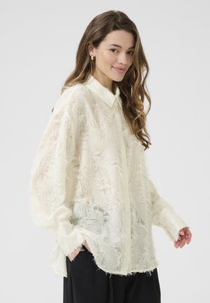 Camicia color crema con un motivo testurizzato, colletto alla francese e maniche lunghe. Tessuto morbido e leggero con dettagli sfilacciati sparsi.