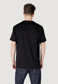 Zwarte T-shirt met korte mouwen van katoen; ronde hals; soepele stof; gecombineerd met donkerblauwe jeans met achterzakken.