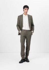 Olive green suit with a tailored fit, paired with a white shirt. Smooth fabric texture, black shoes, and slim-cut trousers.