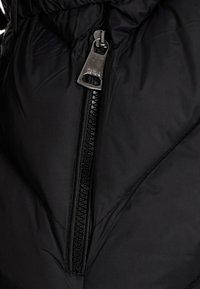 Schwarze gepolsterte Jacke mit diagonalem Reißverschluss. Der Reißverschluss hat einen Metall-Zipfel und eine strukturierte Stoffoberfläche.