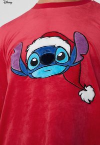 Rotes Plüsch-T-Shirt mit großem, besticktem Motiv eines blauen Charakters mit Weihnachtsmütze. Kurze Ärmel und runder Ausschnitt.