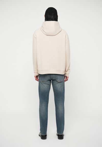 Kremveida kapuce ar brīvā stila piegriezumu, ar lielu kapuci un ribotām aprocēm. Apvienots ar gaiši ziliem džinsiem un melniem apaviem.