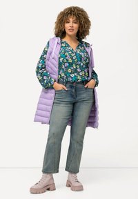 Laventeli puffer-liivi kukkakuosisella puserolla, jossa on vihreän, sinisen ja purppuran sävyjä. Haalistuneet siniset farkut ja vaaleanpunaiset nilkkurit. Teksturoitu kihara tukka.