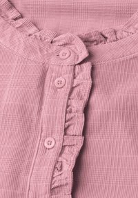 Tissu rose texturé avec fermeture à boutons sur le devant et bordure à volants le long des boutons et du col.