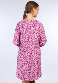 Floral dress featuring a pink background with white and light pink flowers, relaxed fit, long sleeves, and a cinched waist detail.