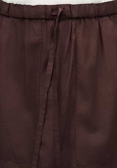 Hnedé látkové nohavice s elastickým pásom a dlhým sťahovacím šnúrkou v strede vpredu, s viditeľnými švami a bočnými vreckami.