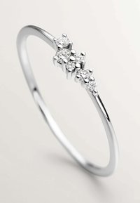 Anillo delgado de plata con grupos asimétricos de piedras preciosas redondas y claras de diferentes tamaños, engastadas en una banda pulida.