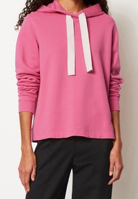 Roze hoodie met een voorzak, witte trekkoorden, geribbelde manchetten en een losse pasvorm, gecombineerd met zwarte broek. Zachte katoenkwaliteit.