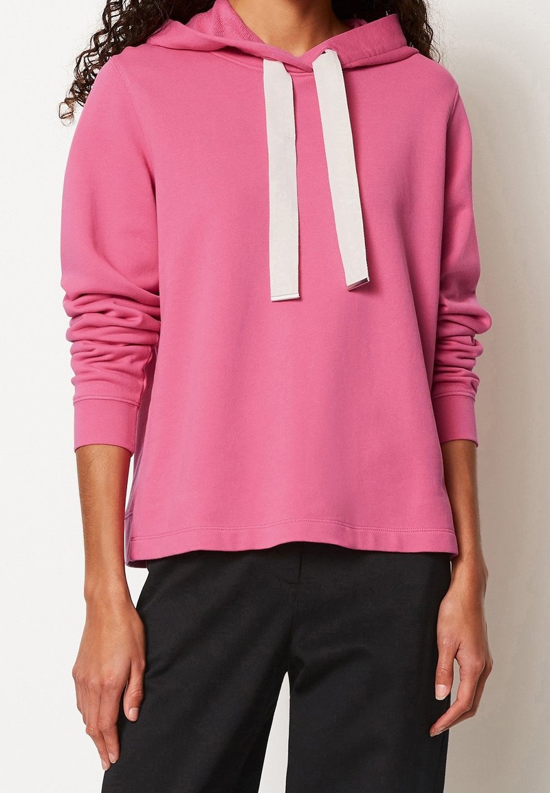 Roze hoodie met een voorzak, witte trekkoorden, geribbelde manchetten en een losse pasvorm, gecombineerd met zwarte broek. Zachte katoenkwaliteit.