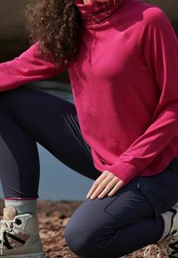 Top de manga larga rosa con cuello alto, combinado con pantalones azul oscuro. Textura suave, ajuste ergonómico, que exhibe costuras mínimas y un diseño atlético.