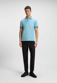 Hellblaues Poloshirt mit schwarz-weißen gestreiften Bündchen, kombiniert mit schwarzen Hosen und schwarzen Sneakers, entworfen für einen enganliegenden Look.